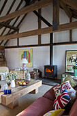 Kissen auf rosa Sofa mit niedrigem Couchtisch und beleuchtetem Holzofen in Camber cottage East Sussex England UK