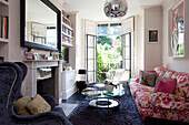 Rosa geblümtes Sofa und Glastisch mit offenen Fenstertüren im Wohnzimmer eines Londoner Stadthauses, England, Vereinigtes Königreich