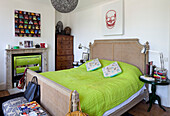 Lindgrüne Bettdecke mit Holztruhe und bunten Kunstwerken im Schlafzimmer eines Londoner Stadthauses, England, UK