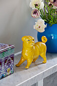 Gelbe Hundestatue mit blauer Vase und Schnittblumen auf einem Regal in einem Haus in London, England, UK