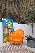 Bright orange armchair with seaside cut-out board in brick courtyard of London home, England, UK