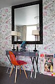 Red plastic chair at side table with matching lamps and large mirror in London home, England, UK