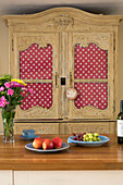Spotted fabric in kitchen dresser with fruit and cut flowers on wooden workbench in UK home