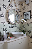 Floral patterned wallpaper with rope mirror above washbasin in UK home