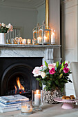 Schnittblumen mit brennenden Kerzen und Feuer im Wohnzimmer eines Hauses in Hertfordshire, England, UK