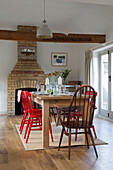 Hölzerner Esstisch mit bemalten Stühlen und freiliegender Backsteinschornstein in einem Londoner Haus, England, UK