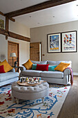 Cup on ottoman footstool with colourful cushions and framed prints in Surrey home,  England,  UK