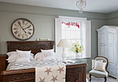 Large clock above wooden carved bed in Berkshire home,  England,  UK