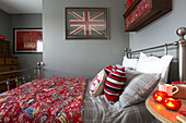 Striped cushions with patterned red quilt on silver wrought iron bed in grey bedroom with Union Jack in Surrey bedroom   England   UK