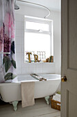 Freestanding bath with floral shower rail at window in Norfolk home England UK