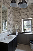 Marble washbasin with large mirror in wallpapered bathroom of Sussex country house England UK