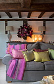 Kerzen und Blumen auf Sideboard mit goldenen und rosa Kissen auf grauem Sofa im Wohnzimmer in Surrey, England UK