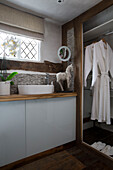 Washbasin below leaded glass window with bathrobe hanging in bathroom of Surrey home England UK