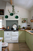 Decorative plates and copper pots in light green fitted kitchen of Dorset home England UK