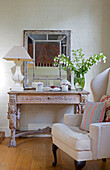 Cut flowers and lamp with mirror on carved table with wingback armchair in West Sussex home England UK