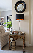 Convex mirror above side table with silver lamp in London townhouse apartment UK