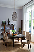 Cream dining chairs at dining table below pendant light in London townhouse UK