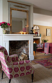 Rosa gepolsterter Sessel am Kamin mit brennenden Kerzen in einem Haus in Sussex, England UK