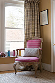 Pink upholstered armchair at sash window in Sussex home England UK