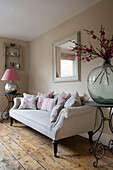 Large glass vase and lamp on side tables with upholstered vintage sofa in Sussex home England UK