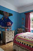 Ethnic dress displayed above chest of drawers with patchwork cover on bed in room of Sussex home England UK