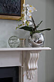Flowering orchid in metallic pot with glass paperweight on mantlepiece in London townhouse England UK