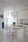 White leather bar stools at breakfast bar with pendant light made from wineglasses in London townhouse England UK