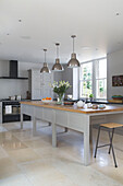 Brushed stainless steel pendant lights above long wooden table in Gloucestershire home England UK