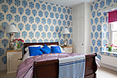 Blau gemusterte Tapete über einem Holzbett mit passenden Nachttischlampen in einer Wohnung in Gloucestershire, England, UK