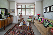 Wooden sideboard and step ladder with bright scatter cushions on sofa in London living room England UK