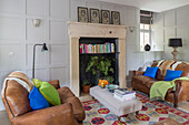 Fireplace repurposed as bookshelf with brown leather two-seater sofas in Gloucestershire living room England UK
