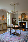 Polished antique table on rug with lit fire and gilded decorative mirrors in Kent country house England UK