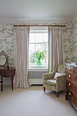 Armchair at window of Georgian bedroom with wooden furniture in Northamptonshire England UK