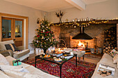 Beleuchteter Baum und Feuer mit Weihnachtsgeschenken im Wohnzimmer in Cheshire, Großbritannien