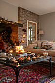 Lit candles and satsumas with pinecones on glass topped coffee table in Cheshire living room UK