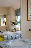 Lilies and berries reflected in bathroom mirror with marble sink in Dorset farmhouse UK