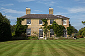 Terrace on lawn with facade of detached Sussex country house England UK