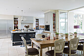 Dining chairs at wooden table in open plan kitchen with island unit and bookshelves in detached Sussex country house UK