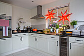 Zwei beleuchtete Sterne mit Dunstabzugshaube und Backofen aus Edelstahl in einer weißen Einbauküche in einem Londoner Stadthaus UK