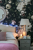 Lamp and lit candle on bedside cabinet with floral wallpaper in Hove apartment East Sussex UK
