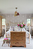 Cut flowers on wooden chest of drawers with metal framed bed in detached 1950s house Alford Surrey UK