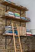 Wandregale und Bücher mit Leiter an einer freiliegenden Ziegelwand in einem umgebauten Schulhaus in Südlondon UK