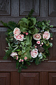 PInk roses with green bow in Christmas wreath on front door of 1930s Arts and Crafts home West Sussex UK