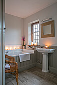 Square mirror above pedestal basin with tongue and groove bath at window in Arts and Crafts home West Sussex UK