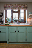 Green cupboards below leaded glass window in kitchen of Hampshire home