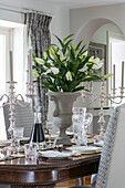 Cut lilies and silver candlesticks on antique dining table in Wiltshire home England UK