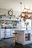 Bar stool at island unit with hanging pans and utensils in Devon kitchen UK
