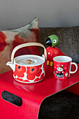 Teetasse und Spielzeug mit Tasse auf leuchtend rotem Frühstückstablett in einem Haus in Nordlondon (UK)