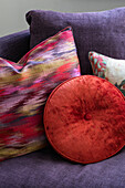 Rote und gemusterte Kissen auf violettem Sofa in einem Haus im Norden Londons (UK)