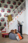 Dog on blanket with umbrella stand in entrance hallway with with large floral motif wallpaper in North London home UK